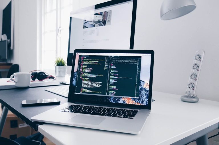 A laptop on a desk with a keyboard and mouse displaying programming code