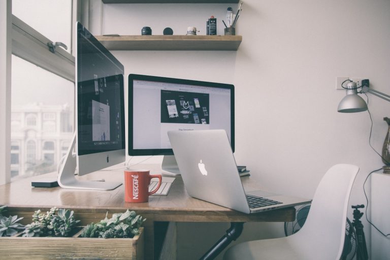 A desk with two computers, a laptop and a coffee cup, creating a productive workspace